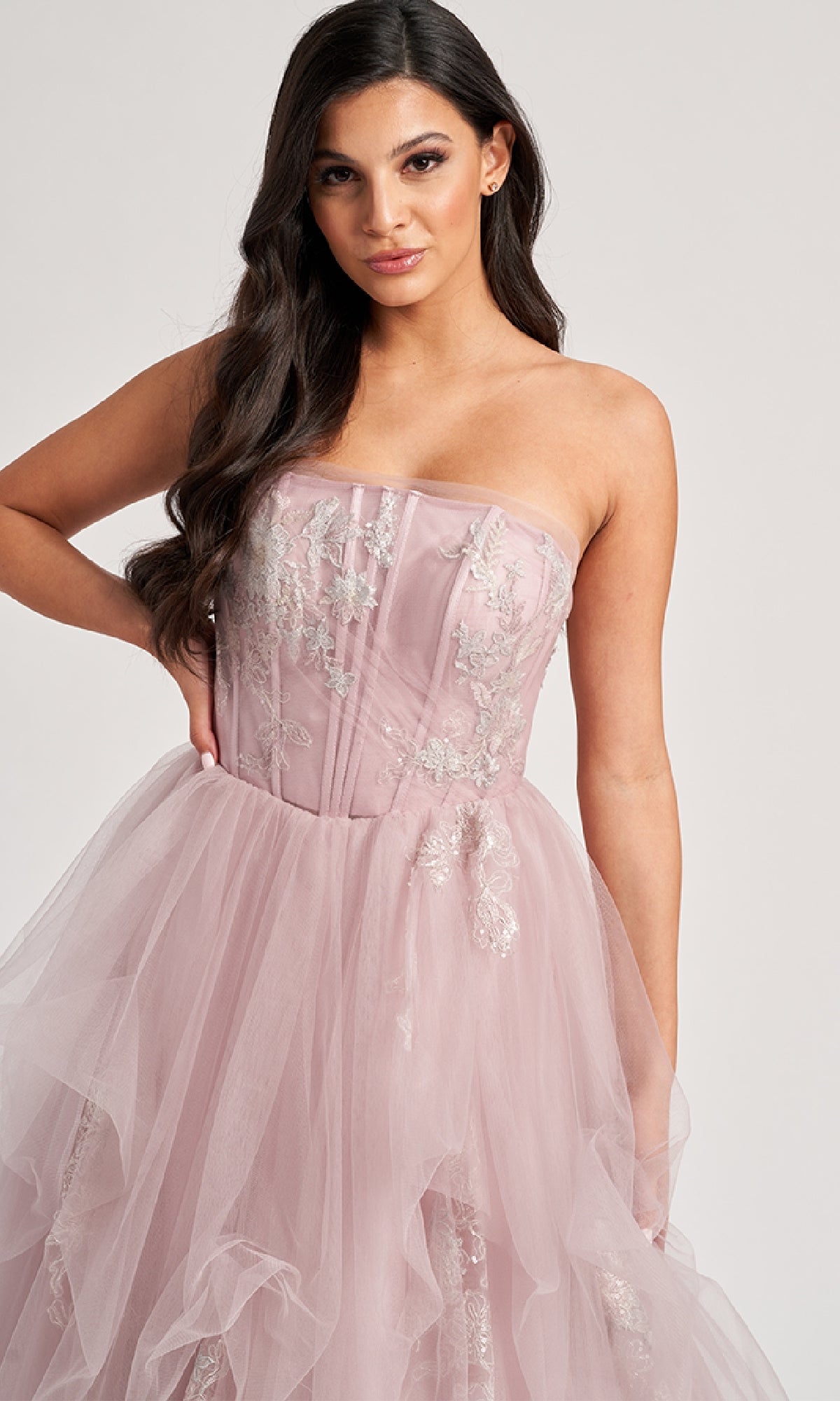 A woman wearing the Colette CL8120 long prom dress, featuring a strapless blush pink A-line tulle skirt and silver floral embroidery, stands against a plain background.